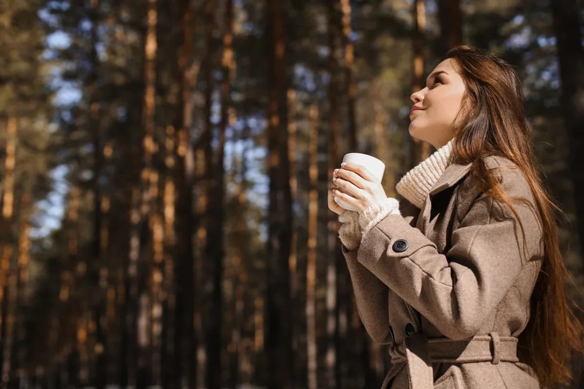 Une femme, une tasse à la main, respire calmement au milieu des arbres
